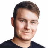 Junger Mann mit kurzen braunen Haaren und heller Haut im schwarzen Hemd, lächelnd vor weißem Hintergrund.
